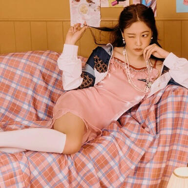 an orange Heng:garae photocard of Mingyu sitting on a bed, leaning against a wall, and smiling at the camera