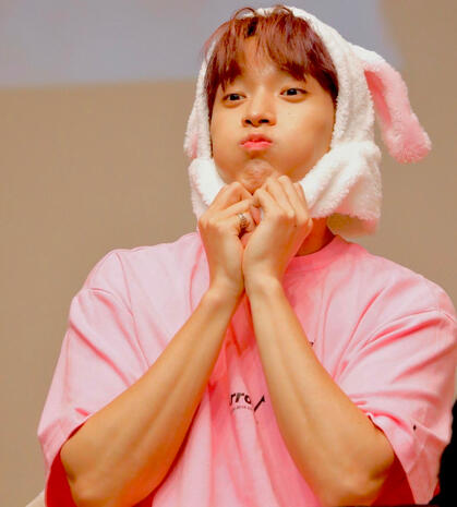 an orange Heng:garae photocard of The8 sitting atop a car, resting his head and hands on his knees and looking at the camera